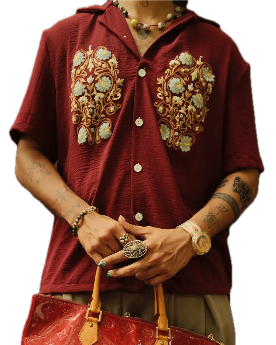Person wearing a maroon textured crepe shirt with intricate Aari embroidery on both sides of the chest, holding a glossy red tote bag.