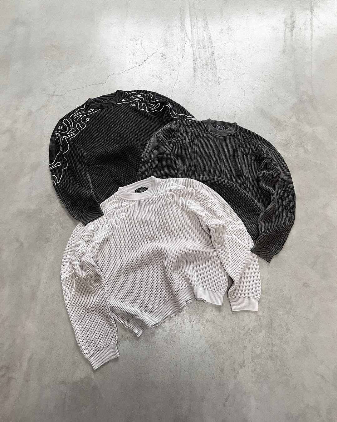 Black and white sweatshirts with decorative patterns on a gray surface