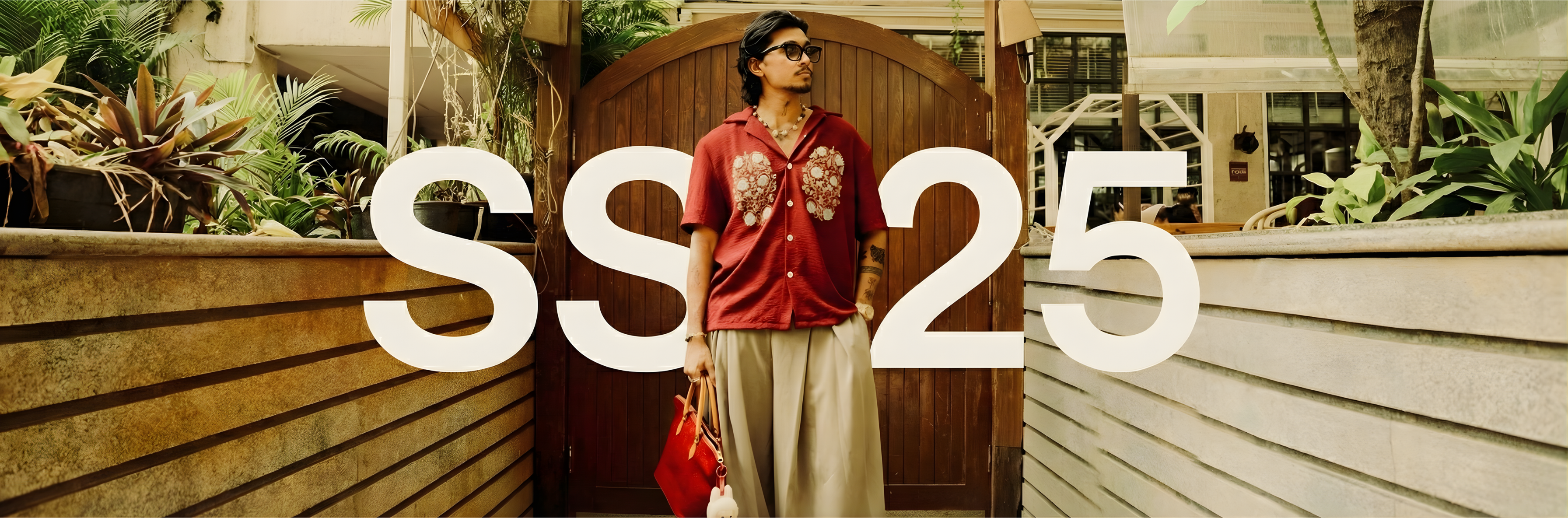 Person holding a red bag with 'SS25' text in front of a wooden door.