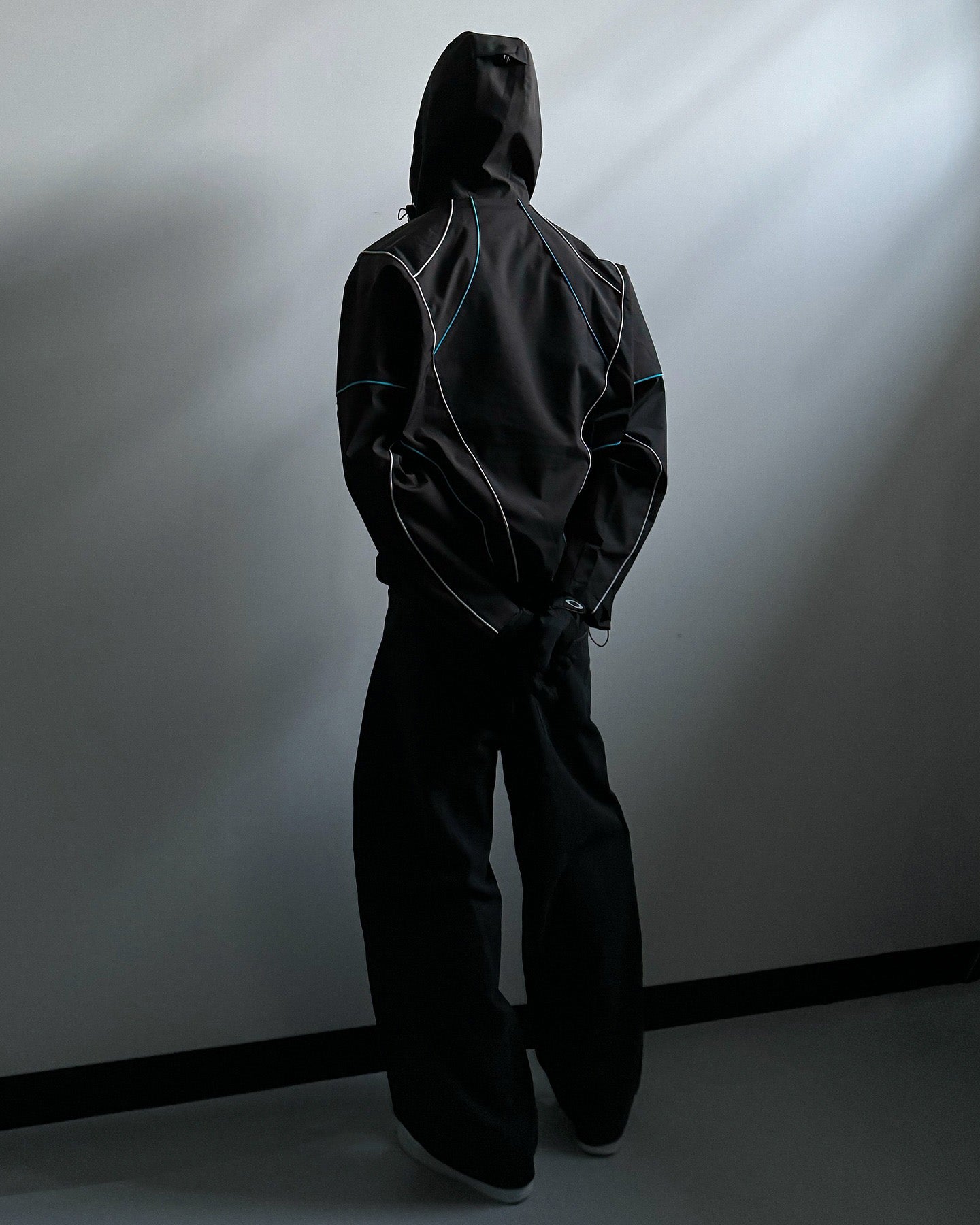 Person wearing a black hooded outfit against a plain background