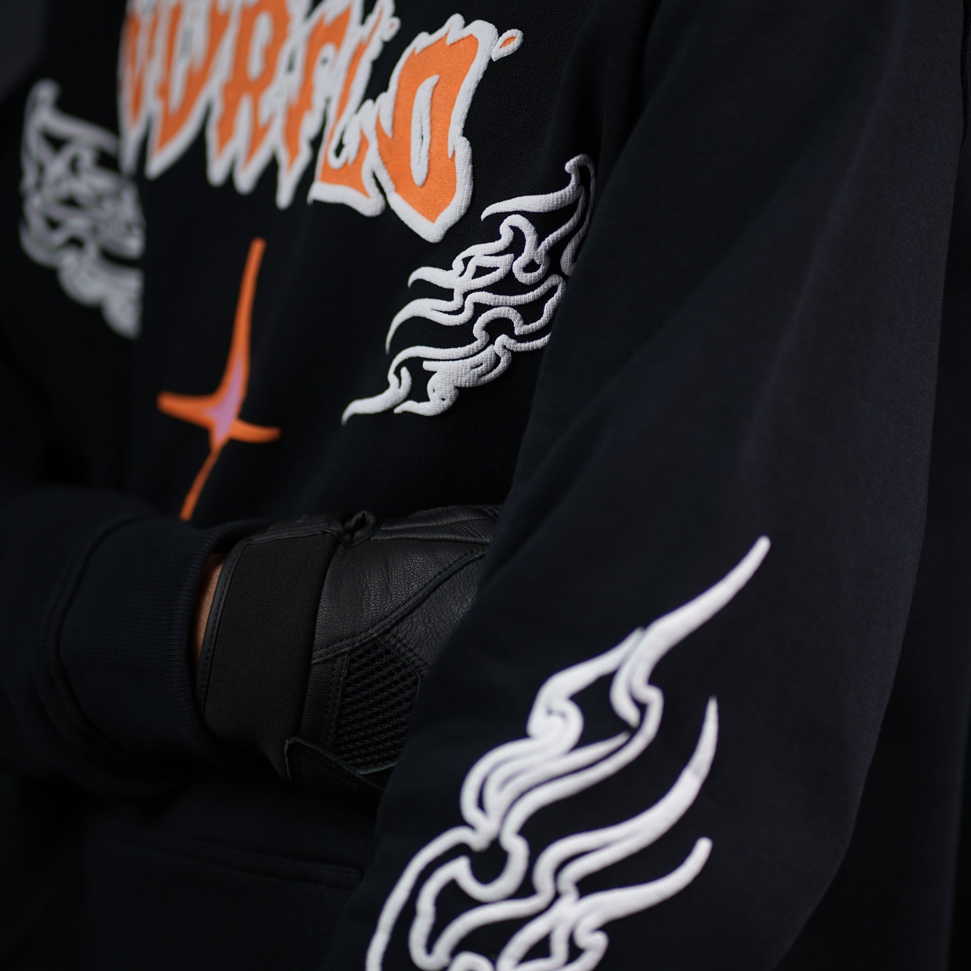 Close-up of NVRFLD black graphic hoodie with orange text and white flame designs on sleeves